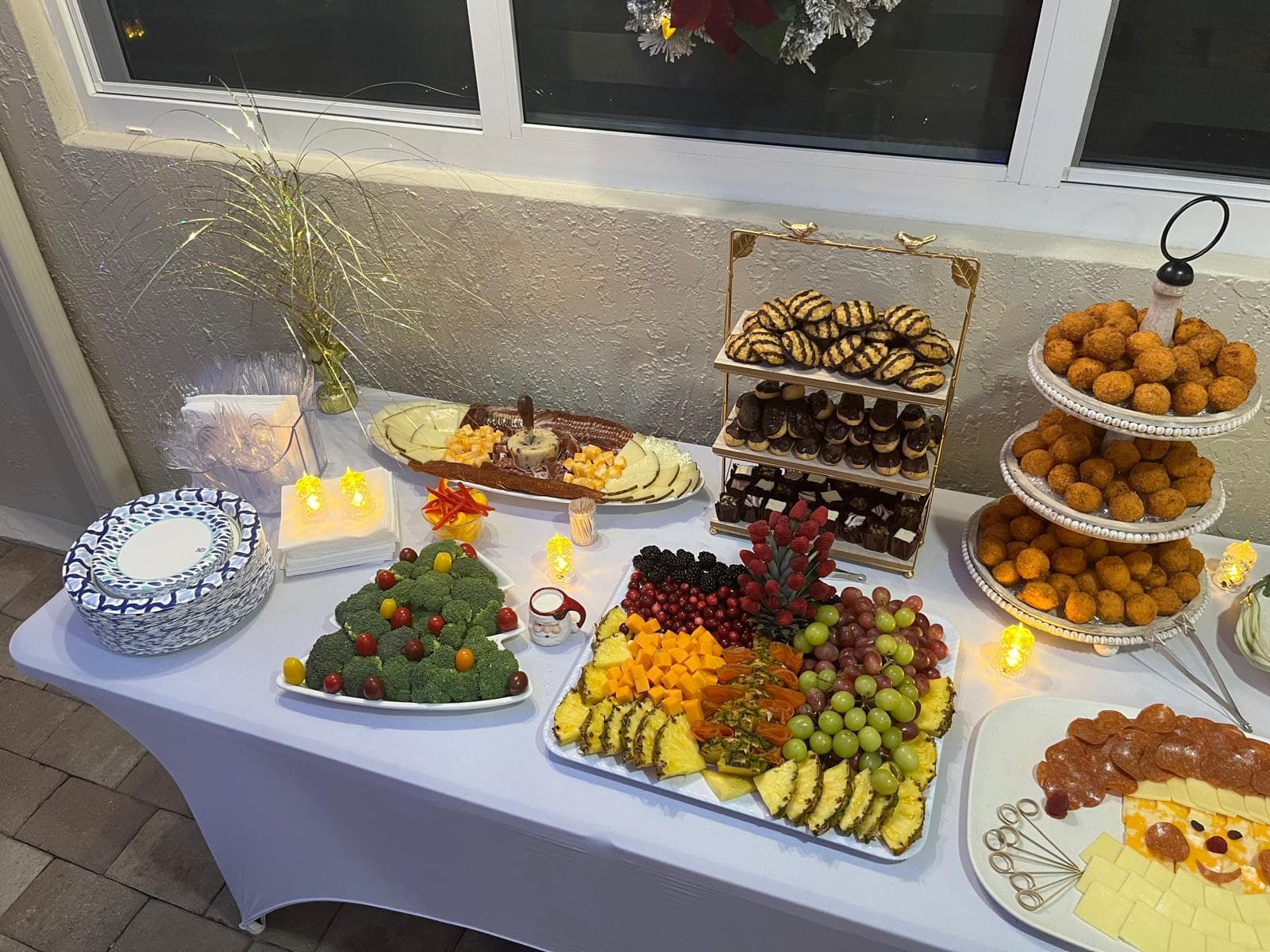 Wide view of a holiday catering spread with a veggie tree, fruit platter and dessert stands