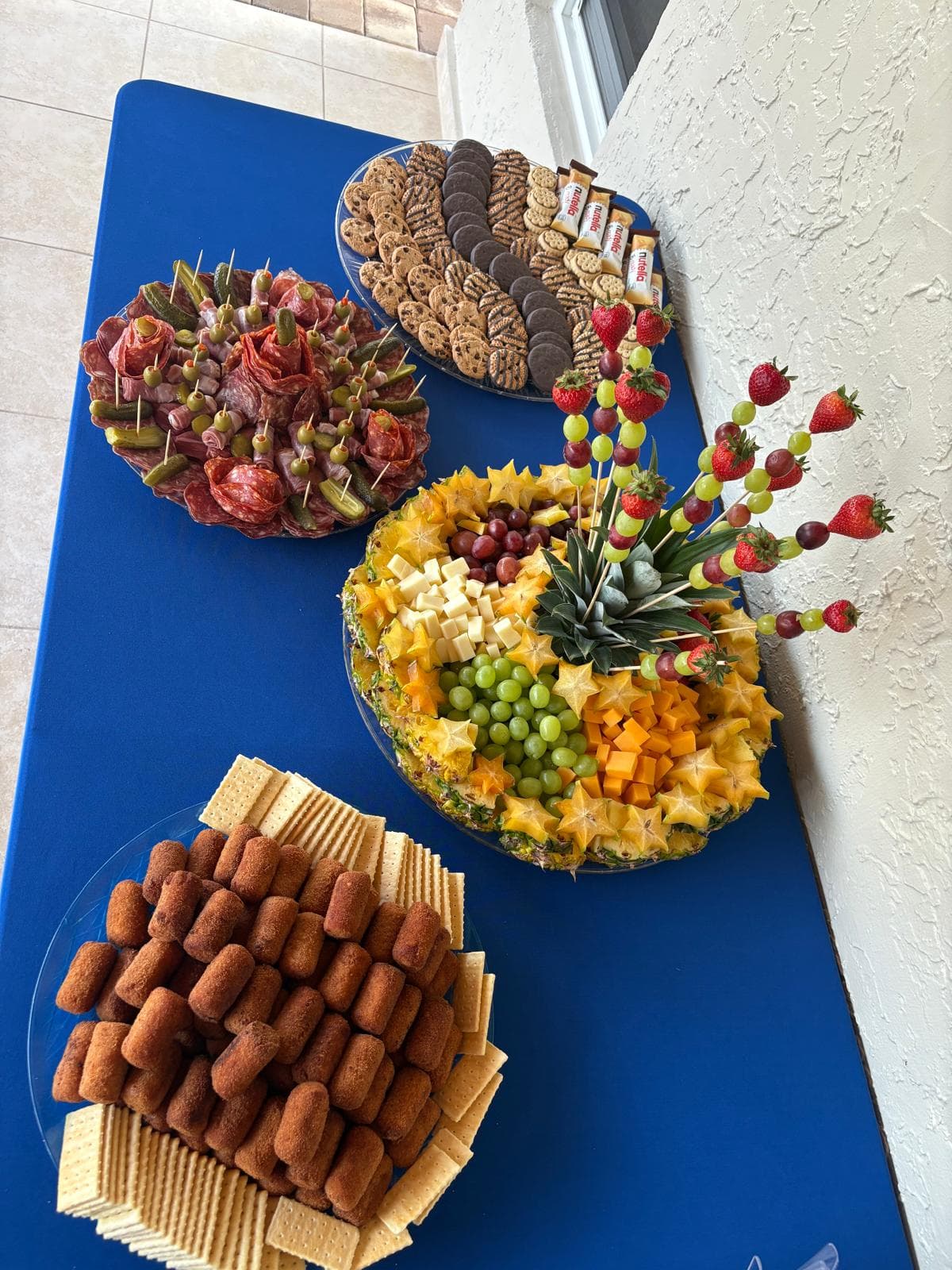 Catering table with a salami rose platter, cookie tray, fruit platter and croquettes