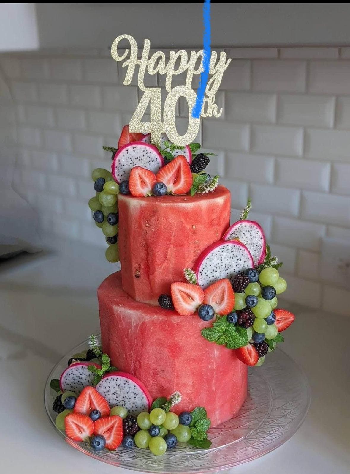 Two-tier carved watermelon fruit cake decorated with berries and a Happy 40th topper