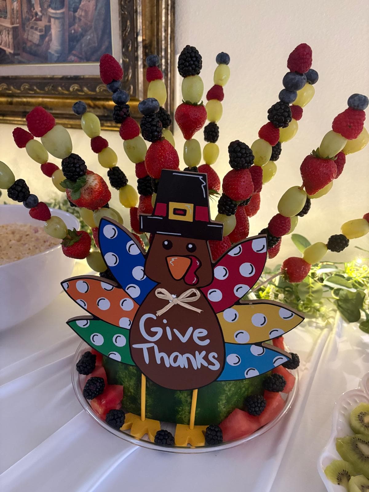 Turkey-shaped fruit skewer display with berries and grapes and a Give Thanks sign on a watermelon base
