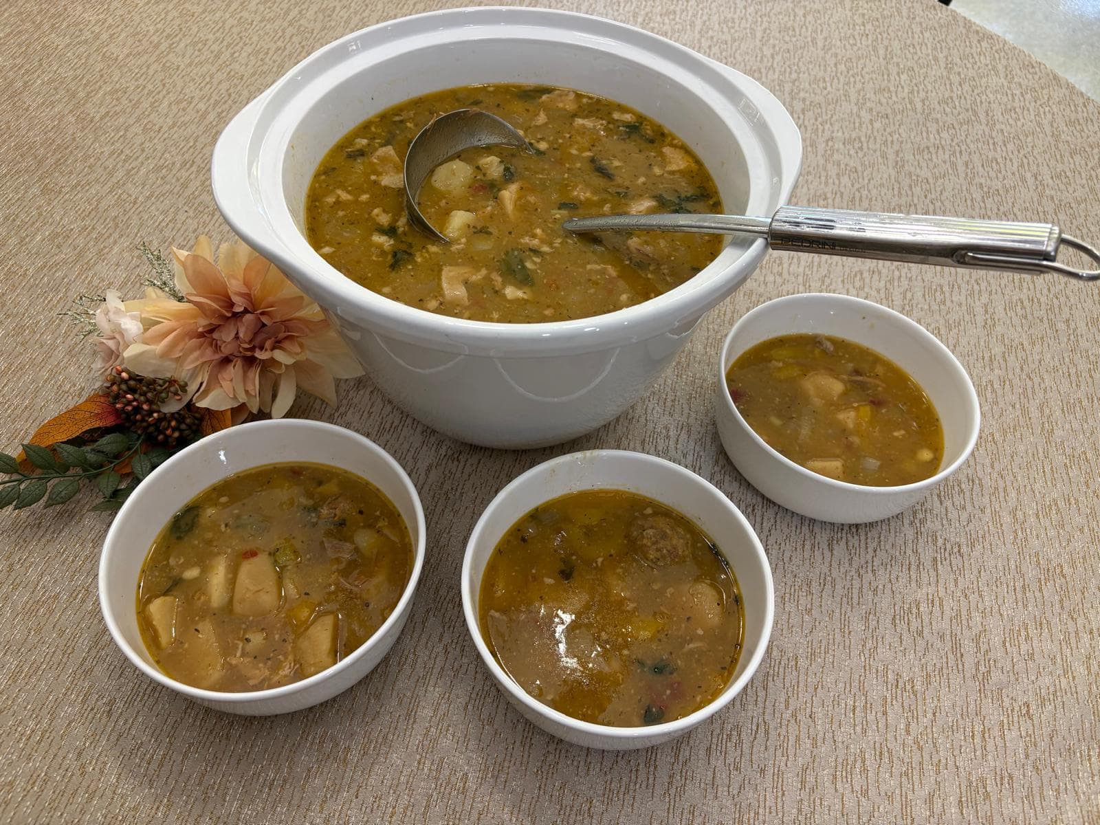 Large tureen of chicken soup with potatoes, tomatoes and herbs served alongside individual bowls
